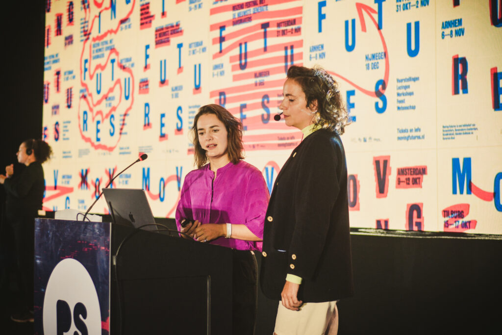 Duas pessoas em um palco apresentando conteúdo durante evento, com tela de fundo e microfones, ilustrando sessões do edital de conteúdos.